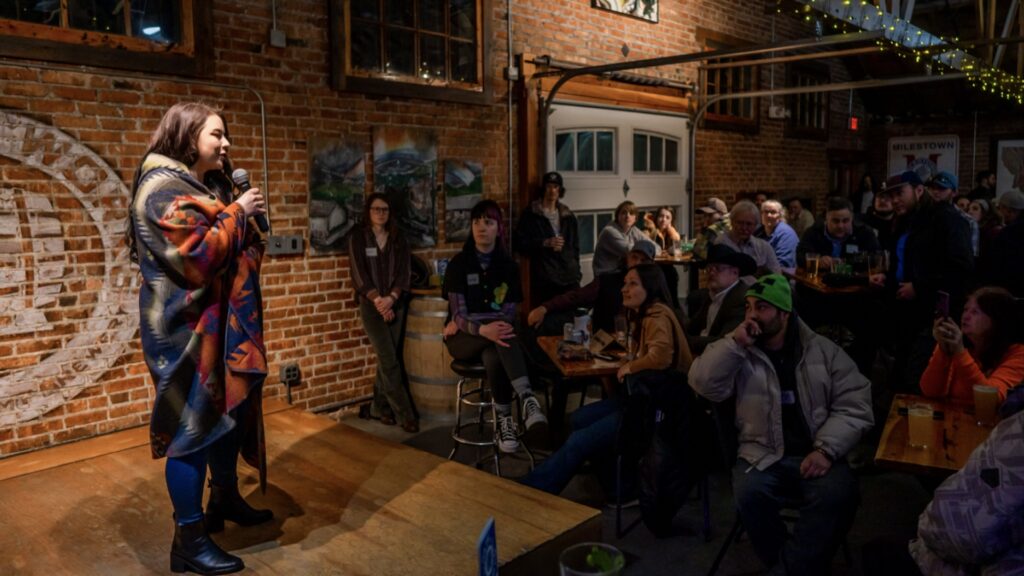 a young woman in a huge coat introduces herself to the crowd at the Lovers Cup